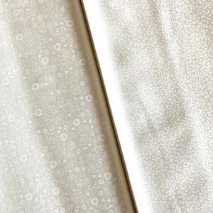Peut inclure: Deux rouleaux de tissu beige avec des motifs floraux et de feuilles blancs. L'un présente de petites fleurs détaillées et des formes géométriques, l'autre un motif de feuilles délicat. Le tissu est probablement en coton ou en lin.