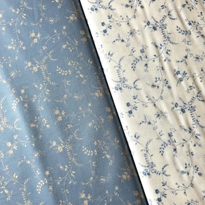 May include: Two fabric samples with floral patterns. One is a pale blue fabric with gold floral vines. The other is an off-white fabric with blue floral vines. Both fabrics are folded, showing the pattern.