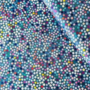 Puede incluir: Primer plano de una tela con un fondo verde azulado oscuro cubierto con un patrón de lunares coloridos. Los lunares son en tonos de blanco, rosa, amarillo, naranja, azul y verde. La tela está doblada, mostrando la textura y el patrón.