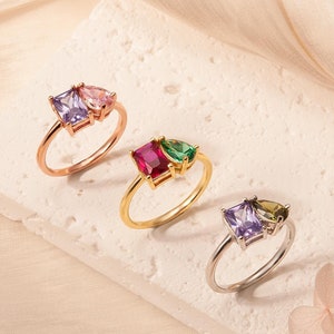 May include: Four rings with different colored gemstones. The rings are on a white surface. The rings are made of gold and silver.