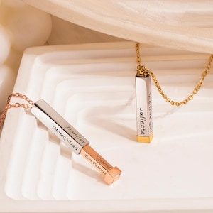 May include: Two vertical bar pendant necklaces with delicate chains. One silver-toned bar is partially extended to reveal a rose gold-toned section, engraved with 'Jennifer', 'Mom heart Dad', and 'David', 'Best Parents'. Another gold-toned bar reads 'Juliette'.