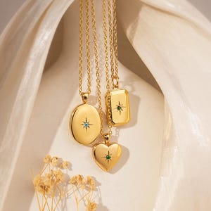 May include: Three gold-toned necklaces featuring pendants in oval, rectangular, and heart shapes. Each pendant is polished and displays a central starburst engraving with a small embedded gemstone. The necklaces hang from delicate gold-toned chains.