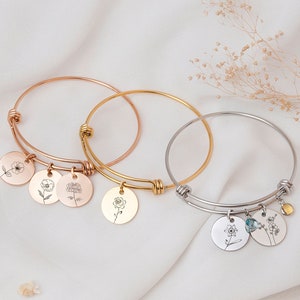 May include: Three delicate bangle bracelets with floral charms. The bracelets are made of gold, rose gold, and silver. Each charm features a different floral design.