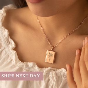 May include: Rose gold rectangular pendant necklace with a delicate rose illustration. The pendant hangs from a matching chain. The image shows the necklace on a person wearing a white blouse.