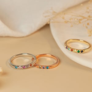 May include: Three dainty rings with colorful gemstones set in a row. The rings are in silver, rose gold, and gold.