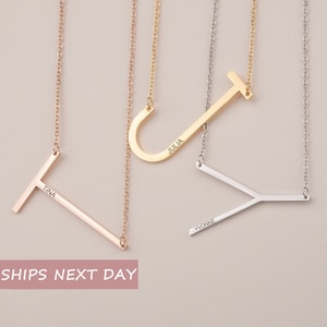 May include: Three personalized initial necklaces in rose gold, gold, and silver. Each necklace features a large letter pendant with a name engraved on it. The letters are connected to a delicate chain.