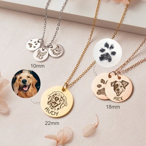 May include: Three silver necklaces with round pendants featuring dog paw prints and dog portraits. The pendants are 10mm, 18mm, and 22mm in diameter. The necklaces are on a white surface with pink flowers.