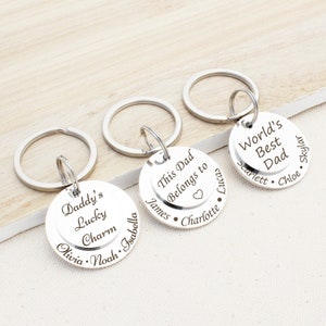 May include: Three silver keychains with engraved round tags. The top tag reads "World's Best Dad" with the names Scarlett, Chloe, and Skylar. The middle tag reads "This Dad Belongs to" with the names James, Charlotte, and Lucas. The bottom tag reads "Daddy's Lucky Charm" with the names Olivia, Noah, and Isabella.