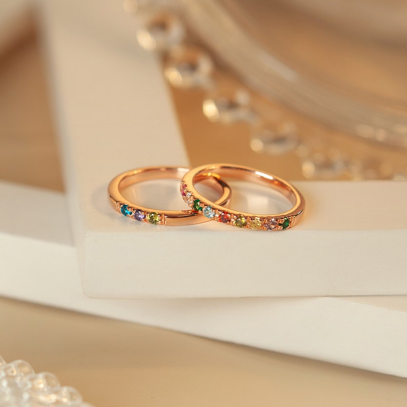 May include: Two thin gold rings with colorful gemstones set in the band. The rings are stacked on top of each other.