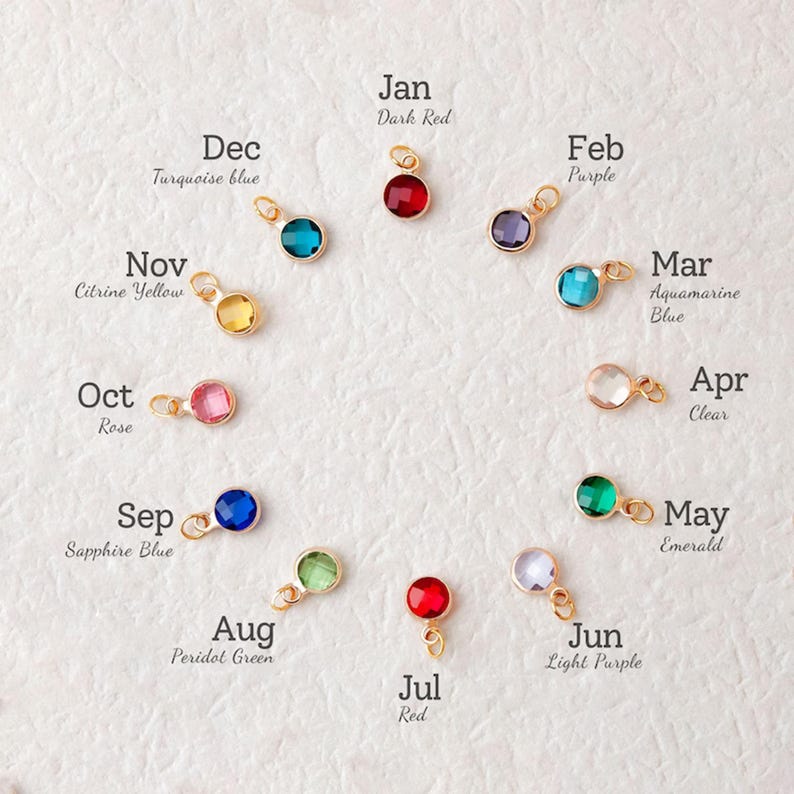 Puede incluir: Una colecci&oacute;n de colgantes dorados, cada uno con una piedra preciosa de diferente color. Las piedras preciosas est&aacute;n dispuestas en c&iacute;rculo, cada piedra est&aacute; etiquetada con un mes y un color, incluyendo Rojo Oscuro, Azul Turquesa, Amarillo Citrino, Rosa, Azul Zafiro, Verde Peridoto, Rojo, P&uacute;rpura, Azul Aguamarina, Claro, Lila Claro y Esmeralda.