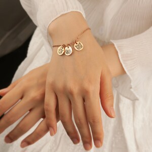 May include: Rose gold charm bracelet featuring three round pendants with engraved animal portraits. The bracelet is worn on a wrist, showcasing the delicate chain and the detailed designs of the charms. The bracelet is a piece of jewelry.