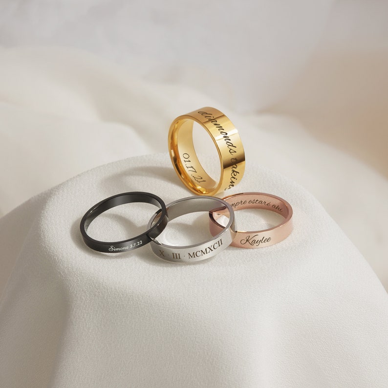 May include: Four different engraved rings. The rings are gold, silver, black, and rose gold. The engravings include "Diamonds are forever", "Simone 3.7.22", "X.III.MCMXCI", and "Kaylee".