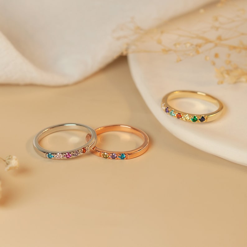 May include: Three dainty rings with colorful gemstones set in a row. The rings are in silver, rose gold, and gold.