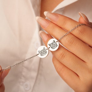 May include: A silver chain necklace with two round pendants featuring engraved images of cats' faces.