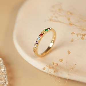 May include: A gold band ring with a row of colorful gemstones. The gemstones are red, orange, yellow, green, blue, and purple.