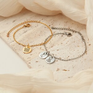 May include: Two delicate bracelets. One is gold-toned with a round charm featuring a cat's face. The other is silver-toned with two round charms, each with a rabbit design. Both bracelets have adjustable chain closures.