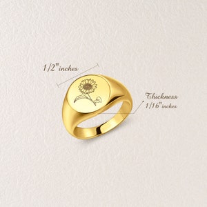 May include: A gold signet ring with a sunflower design engraved on the top. The ring is 1/2" in diameter and 1/16" thick.