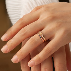 May include: Two gold rings with colorful gemstones. The top ring has five small gemstones in a rainbow pattern. The bottom ring has three larger gemstones in yellow, pink, and purple.