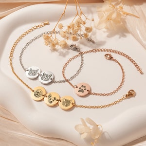 May include: Three gold, silver, and rose gold chain bracelets with charms. The gold bracelet has three round charms with engraved images of a dog, a cat, and a dog. The silver bracelet has two round charms with engraved images of a cat. The rose gold bracelet has one round charm with an engraved paw print.