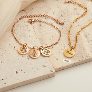 May include: Rose gold bracelet with three engraved pet portraits and a gold necklace with a round pendant. The pendant is engraved with the name "Daisy". The jewelry is displayed on a neutral surface.