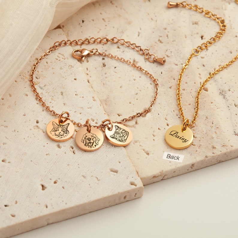 May include: Rose gold bracelet with three engraved pet portraits and a gold necklace with a round pendant. The pendant is engraved with the name "Daisy". The jewelry is displayed on a neutral surface.