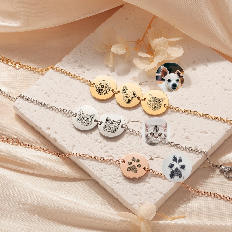 May include: Three silver and gold bracelets with engraved pet portraits and paw prints. The bracelets are layered on a white surface.