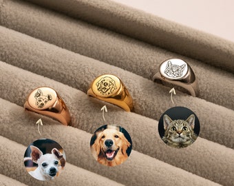 May include: Three signet rings with personalized engravings of pets. The rings are made of gold and silver and feature a dog, a cat, and a dog. The rings are displayed in a velvet-lined box.