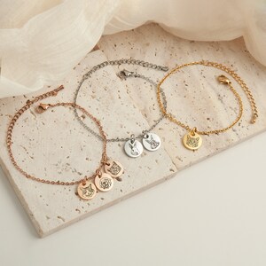 May include: Three delicate bracelets in rose gold, silver, and gold. Each bracelet features a chain with a small, round pendant. The pendants are engraved with pet portraits, including a cat, dog, and rabbit. The bracelets are displayed on a neutral surface.