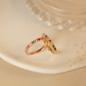 May include: Two gold rings with colorful gemstones set in a row around the band. The rings are stacked on top of each other.