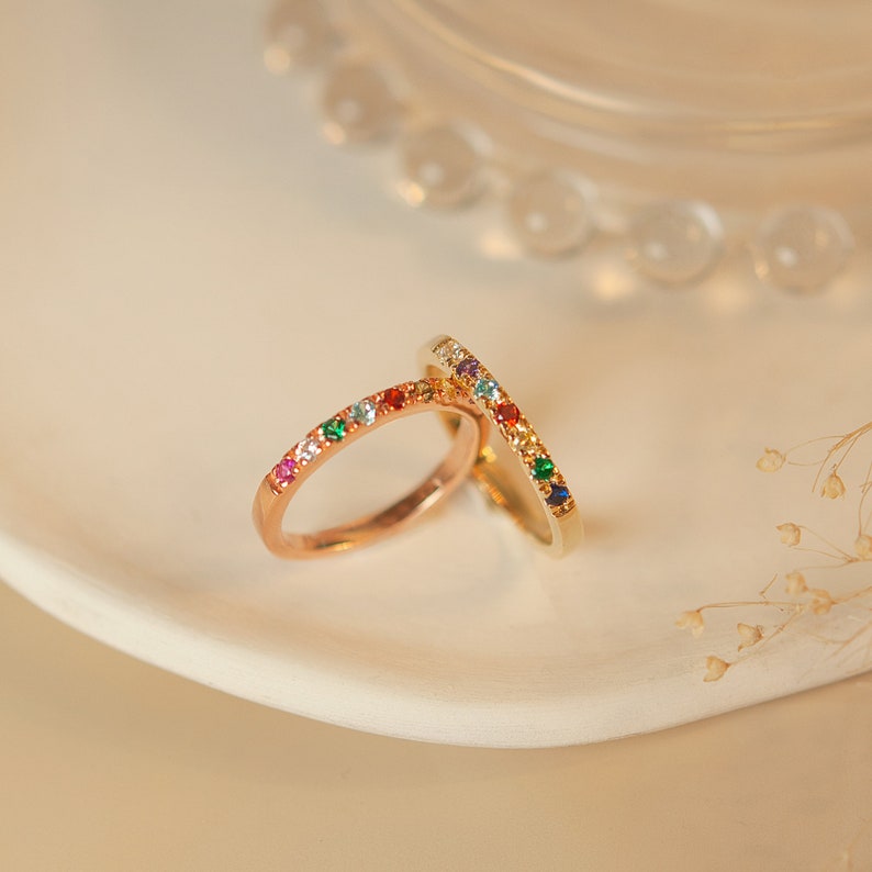 May include: Two gold rings with colorful gemstones set in a row around the band. The rings are stacked on top of each other.