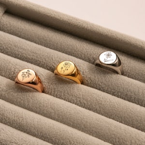 May include: Four gold and silver signet rings with different floral designs. The rings are displayed in a velvet-lined box.