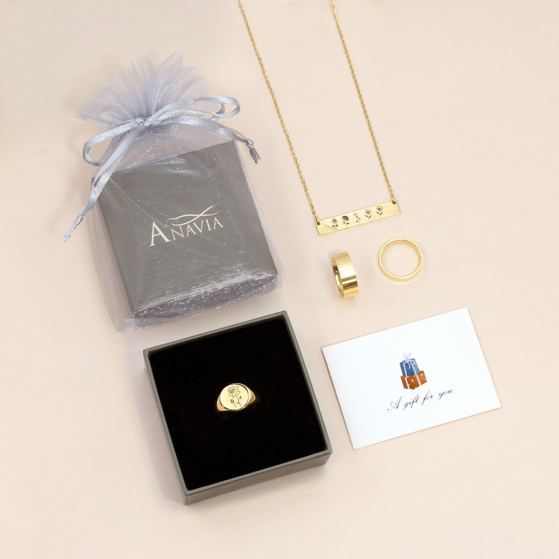 May include: A gift set with a gold ring, necklace, and card. The ring has a rose design. The necklace has a bar pendant with small symbols. The card says "A gift for you".