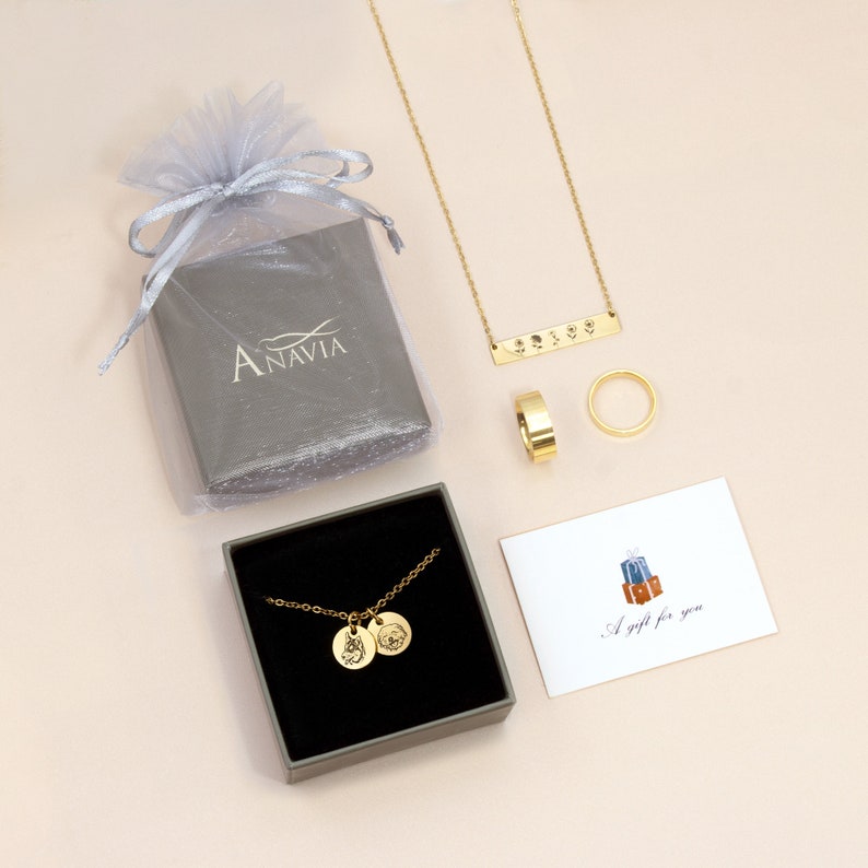 May include: An assortment of gold-colored jewelry, including a necklace, rings, and a pendant necklace with two circular charms. A gift card with the text "A gift for you" is also present, along with a gray gift box and a sheer bag.