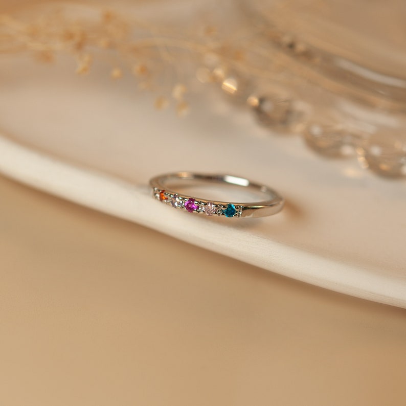 May include: A silver band ring with a row of colorful gemstones. The stones are orange, pink, purple, white, and blue.