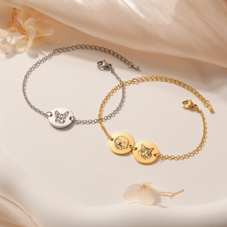 May include: Two personalized pet photo bracelets. One bracelet is silver with a single oval charm featuring a dog's face. The other bracelet is gold with two round charms featuring a dog and a cat's face.