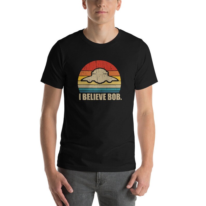 May include: A black t-shirt with a retro-style graphic of a UFO with the text "I BELIEVE BOB." printed on it.