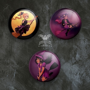 May include: Three round purple and yellow buttons with images of witches flying on broomsticks. The witches are wearing black and purple dresses and hats. The buttons have a white background with black text that reads "Alice Quinn Art Art of the Unusual".