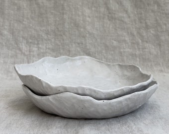 May include: Two white ceramic bowls with a wavy, organic rim. The bowls are stacked on top of each other.