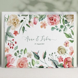 May include: A white wedding invitation with a watercolour floral border. The text reads "Anna & Torben" and "27. August 2021".