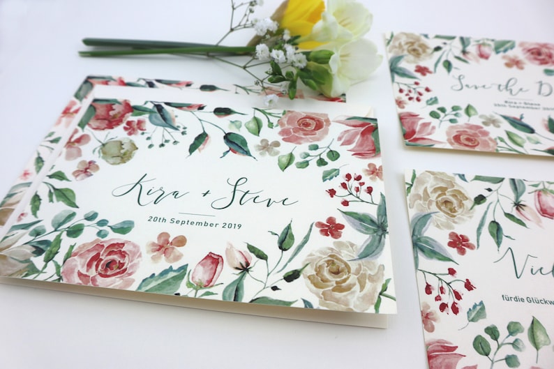 May include: Save the Date cards with a floral design featuring pink, red, and white flowers. The text on the card reads "Save the Date" and "Kira + Steve" with the date "20th September 2019".