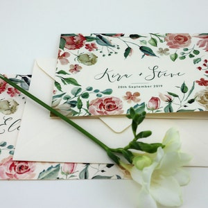 May include: A floral wedding invitation with a watercolour design featuring pink and white roses, green leaves, and the text "Kira & Steve 20th September 2019".