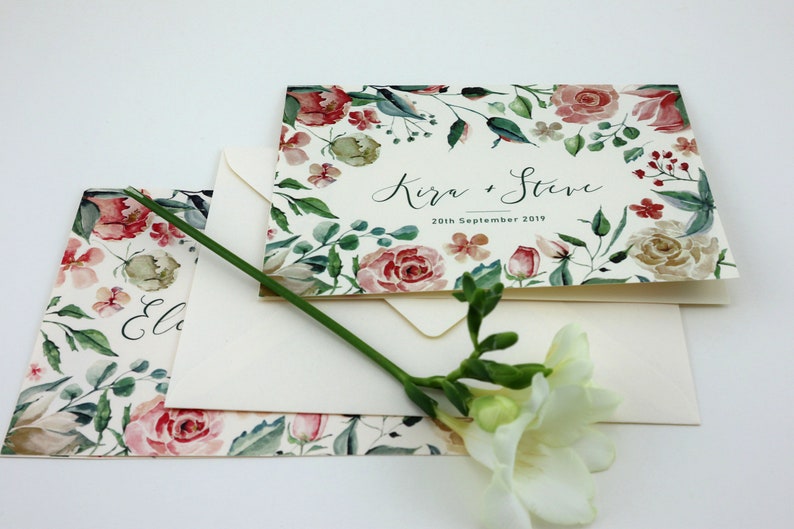 May include: A floral wedding invitation with a watercolour design featuring pink and white roses, green leaves, and the text "Kira & Steve 20th September 2019".