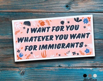 May include: A rectangular card with the text "I WANT FOR YOU WHATEVER YOU WANT FOR IMMIGRANTS" in a bold, stylized font. The card has a pink background with floral and leaf accents in blue, orange, and white. The card is on a blue wooden surface.