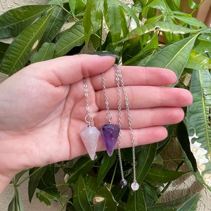 May include: Two crystal pendulums with silver chains. The pendulums are in the shape of a point and are made of rose quartz and amethyst.