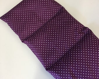 May include: A purple and white polka dot fabric heating pad. The pad is folded in half and is lying on a white surface.