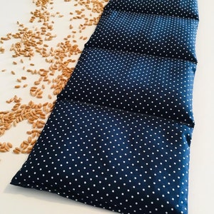 Könnte beinhalten: Ein langer, rechteckiger blauer Heizkissen aus Stoff mit weißen Punkten. Das Kissen besteht aus fünf zusammengenähten Abschnitten. Das Kissen liegt auf einer weißen Oberfläche mit verstreuten Weizenkörnern.