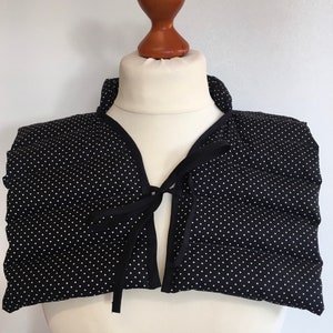 May include: Black and white polka dot neck warmer with a black tie closure. The neck warmer is made of a soft, quilted fabric.