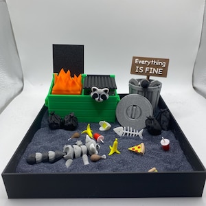 May include: A miniature diorama featuring a raccoon skeleton amidst trash, a green dumpster with flames, and a sign that reads "Everything Is Fine." Includes a pizza slice, bananas, and a fish skeleton.