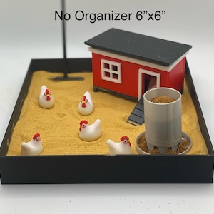 Może przedstawiać: Miniaturowy kurnik z czerwonym zewnętrzem i czarnym dachem stoi na piaskowej podstawie. Pięć białych ceramicznych kur z czerwonymi grzebieniami rozrzuconych wok&oacute;ł kurnika. Podstawa jest otoczona czarną ramą. Tekst "No Organizer 6"x6" jest nadrukowany nad kurnikiem.