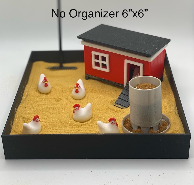 Może przedstawiać: Miniaturowy kurnik z czerwonym zewnętrzem i czarnym dachem stoi na piaskowej podstawie. Pięć białych ceramicznych kur z czerwonymi grzebieniami rozrzuconych wok&oacute;ł kurnika. Podstawa jest otoczona czarną ramą. Tekst "No Organizer 6"x6" jest nadrukowany nad kurnikiem.